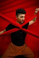 un asiatique homme des stands dans de face de une rouge en forme de X tissu et détient il avec tous les deux mains photo