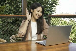 jeune femme asiatique faisant une vidéoconférence sur un ordinateur portable assis au café, ayant une réunion photo