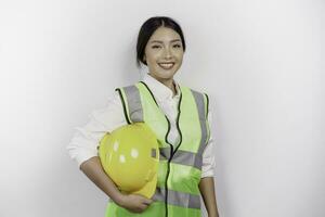 sur de soi asiatique femme la main d'oeuvre ouvrier est souriant à le caméra, apportant sa sécurité casque, portant Jaune sécurité casque, vert gilet et uniforme, isolé blanc Contexte. photo