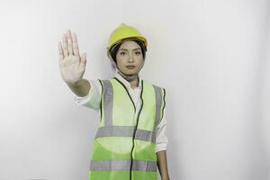 sérieux asiatique femme la main d'oeuvre portant sécurité casque et gilet avec main geste pose rejet ou interdiction, isolé par blanc Contexte photo