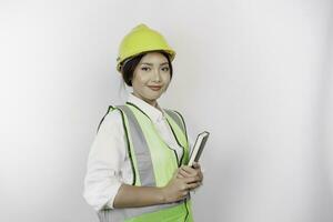 une souriant asiatique femme la main d'oeuvre portant sécurité casque et gilet, en portant sa livre, isolé par blanc Contexte. le travail journée concept. photo