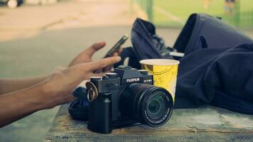 Fujifilm X t30 caméra mis sur une en bois surface avec une sac dans le Contexte et une main en portant une téléphone intelligent. photo