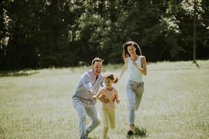 jeune famille heureuse avec une petite fille mignonne qui court dans le parc par une journée ensoleillée photo