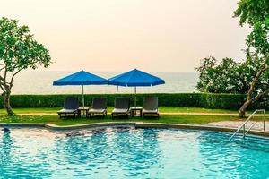 chaises de plage ou lits de piscine avec parasols autour de la piscine au coucher du soleil photo