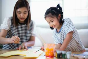 mignon petit enfant peignant avec des peintures colorées. fille asiatique et mère utilisant la couleur de dessin au crayon. fille et maman faisant leurs devoirs à colorier des personnages de dessins animés. concept de mode de vie de l'activité de bébé artiste. photo