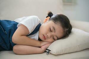 mignonne peu fille enfant en train de dormir sur canapé canapé avec doux oreillers à vivant pièce à maison. bébé fille mensonge sur le canapé canapé lit. photo