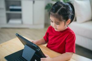 asiatique enfant fille à la recherche en utilisant et toucher tablette afficher filtrer. bébé souriant marrant temps à utilisation tablette. aussi beaucoup écran temps. mignonne fille en train de regarder vidéos tandis que la télé, l'Internet dépendance concept. photo