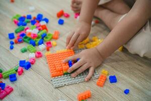 Haut voir. joyeux asiatique fille content et souriant en jouant coloré lego jouets, séance sur le vivant pièce sol, créative en jouant avec légo, bâtiment coloré les structures la créativité imaginer. photo