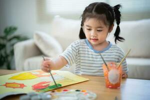 mignon petit bébé asiatique souriant peinture avec des peintures colorées à l'aquarelle. fille asiatique utilisant la couleur de dessin au pinceau. concept de mode de vie d'activité de bébé. photo