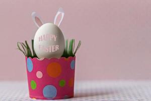 œuf de poule blanc avec oreilles de lapin dans un bac en papier rose écologique, boîte. concept de joyeuses fêtes de pâques. texte anglais joyeuses pâques photo