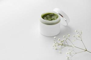 récipient en plastique ouvert avec de la crème et des fleurs sur fond blanc. crème pour le visage. crème aux herbes. produits cosmétiques. mise au point sélective. photo