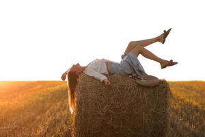 portrait de belle fille sur un rouleau de botte de foin sur un champ de blé récolté en été. mise au point sélective. photo