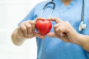 Une patiente asiatique âgée ou âgée tenant un coeur rouge dans sa main sur un lit dans une salle d'hôpital de soins infirmiers, concept médical solide et sain
