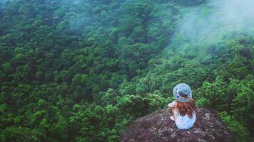 les femmes asiatiques voyagent se détendent pendant les vacances. asseyez-vous sur une falaise rocheuse. bois de nature sauvage sur la montagne. photo