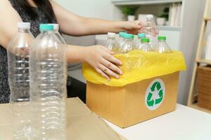 Accueil recycler éco vert zéro concept femme lancement vide Plastique bouteille dans recyclage poubelle avec Jaune des ordures Sacs à maison. photo