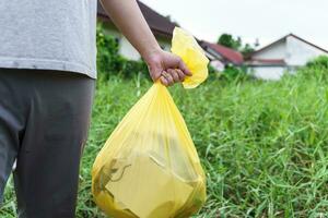 homme bénévole charité en portant des ordures Jaune sac et Plastique bouteille des ordures pour recyclage nettoyage photo
