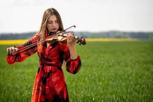 Jeune femme en robe rouge jouant du violon dans un pré vert - image photo