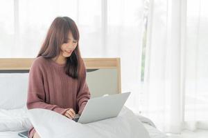 femme asiatique travaillant avec un ordinateur portable sur le lit à la maison photo