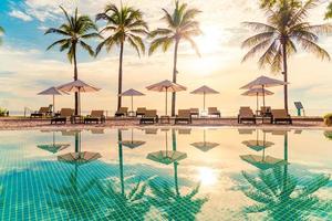 beaux parasols et chaises de luxe autour d'une piscine extérieure dans un hôtel et un complexe avec des cocotiers au coucher du soleil ou au lever du soleil - concept de vacances et de vacances photo