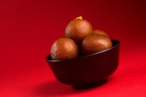 gulab jamun dans un bol noir sur fond rouge. dessert indien ou plat sucré. photo