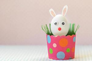 oeuf de poule blanc avec des oreilles de lapin et un museau dans un bac en papier rose respectueux de l'environnement, boîte. concept de joyeuses fêtes de pâques. photo