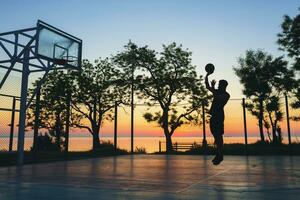 noir homme Faire des sports, en jouant basketball sur lever du soleil, sauter silhouette photo