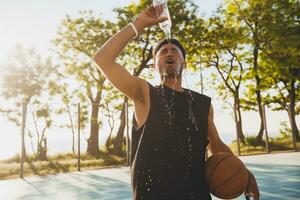 fermer portrait de Jeune noir homme Faire des sports dans matin, en buvant l'eau sur basketball tribunal photo