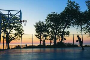 noir homme Faire des sports, en jouant basketball sur lever du soleil, silhouette photo