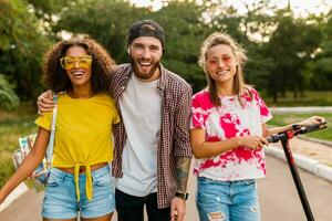 content Jeune entreprise de souriant copains en marchant dans parc avec électrique donner un coup scooter photo