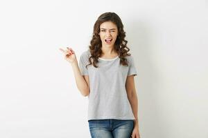 portrait de Jeune attrayant femme habillé dans décontractée tenue T-shirt et jeans, montrer du doigt doigt, un clin d'oeil, souriant, content, branché style, isolé photo