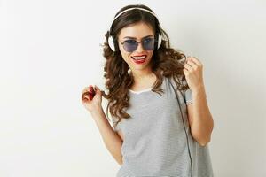 Jeune attrayant femme écoute à la musique sur écouteurs, portant des lunettes de soleil, isolé sur blanc arrière-plan, photo