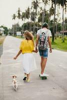 Jeune élégant branché couple dans l'amour sur vacances avec chien et planche à roulette photo