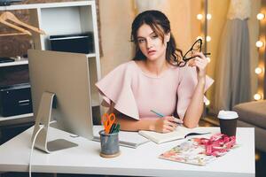 femme dans rose luxe robe, été s'orienter, mode designer travail à Bureau sur ordinateur photo