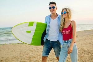 Jeune souriant couple ayant amusement sur plage en marchant avec le surf planche photo