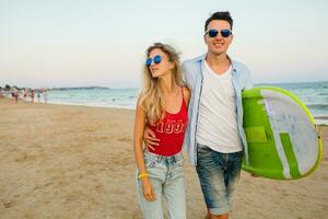 Jeune souriant couple ayant amusement sur plage en marchant avec le surf planche photo