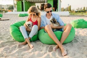 Jeune attrayant souriant couple ayant amusement sur plage en jouant avec chiens photo