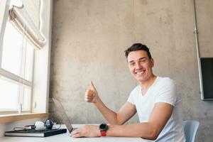 Jeune Beau homme dans décontractée tenue séance à table travail sur ordinateur portable, dactylographie, pigiste à Accueil photo