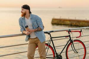 Jeune barbu homme en voyageant sur vélo à le coucher du soleil mer photo