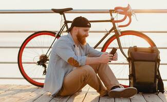 Jeune barbu homme en voyageant sur vélo à le coucher du soleil mer photo