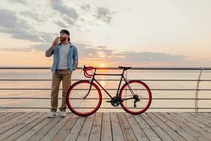 Beau barbu homme en voyageant avec vélo dans Matin lever du soleil par le mer photo