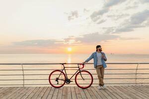 Beau barbu homme en voyageant avec vélo dans Matin lever du soleil par le mer photo