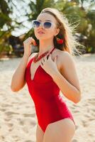 Jeune magnifique blond femme bain de soleil sur plage dans rouge nager costume, des lunettes de soleil photo