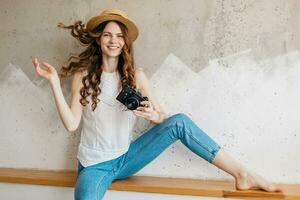 Jeune jolie souriant content femme dans paille chapeau en portant ancien photo caméra, longue frisé cheveux