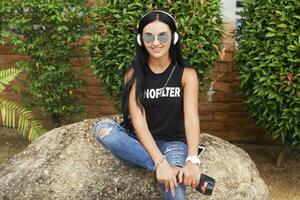 Jeune élégant branché femme dans noir T-shirt, jeans, écoute à la musique sur écouteurs photo