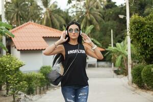 Jeune élégant branché femme dans noir T-shirt, jeans, écoute à la musique sur écouteurs photo