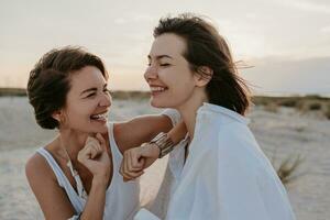 deux Jeune femmes ayant amusement sur le le coucher du soleil plage photo