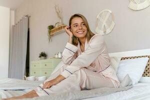 jolie souriant femme relaxant à Accueil sur lit dans Matin dans pyjamas photo