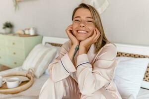 jolie souriant femme relaxant à Accueil sur lit dans Matin dans pyjamas photo