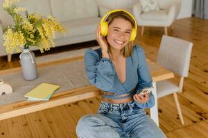 Jeune jolie élégant souriant femme relaxant à Accueil écoute à la musique sur écouteurs photo
