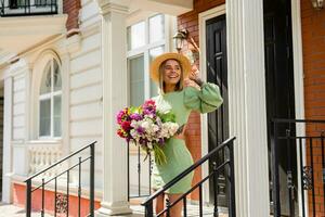 magnifique Jeune femme dans été style tenue souriant content en marchant avec fleurs dans ville rue photo